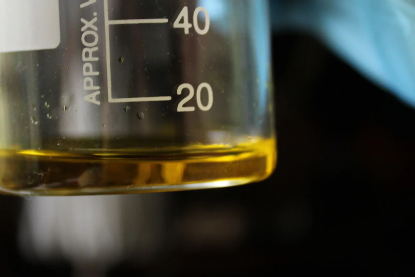 Gloved laboratory technician reviewing an amber oil sample in a beaker