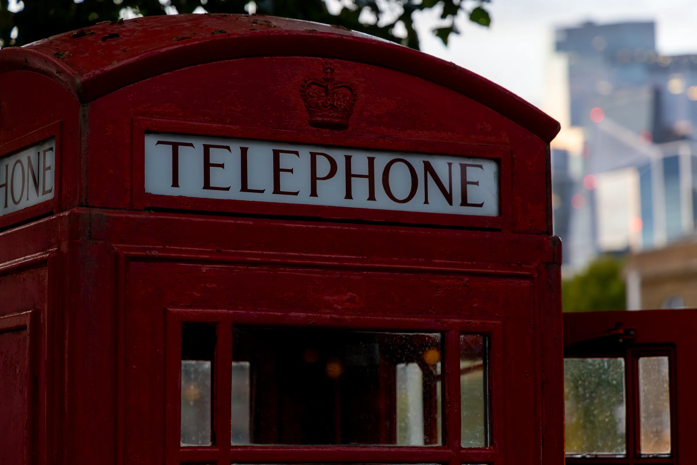 Close-up of a red British telephone box with London's Canary Wharf skyline behind it