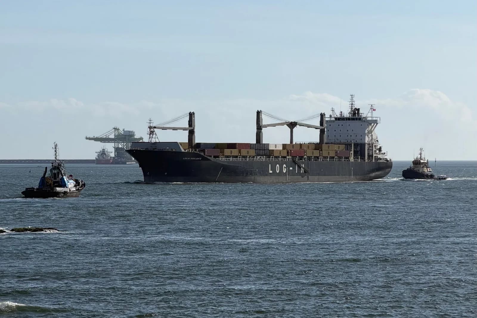 Cargo vessel escorted by tugboats while leaving a working port